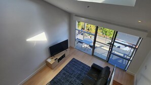A modern living room with a large TV, black leather sofa, and a wooden floor. - Semaphore Blue Apartments (Semaphore)