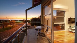 A balcony with a view of the sunset, a table with chairs, and a large window. - Semaphore Blue Apartments (Semaphore)