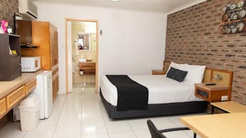 A hotel room with a bed, bedside table, desk, and a brick wall.