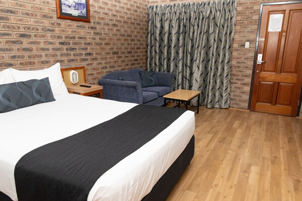 A hotel room with a large bed, a small table, a chair, a wooden door, and a brick wall. - Lantern Motor Inn (West Mackay)