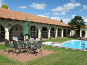 Un área junto a la piscina con mesa y sillas, un porche cubierto y una pileta.