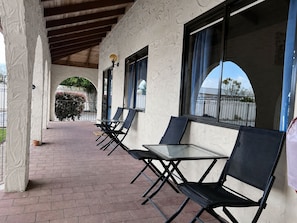 A covered outdoor seating area with tables and chairs, a brick floor, and a view of a fence and trees. - Captains Quarters Motor Inn (Cambridge)
