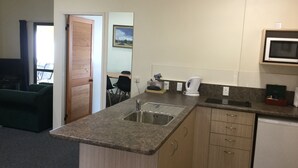 A compact kitchen with a sink, microwave, and a small refrigerator. There is a dining area visible through an open door. - Captains Quarters Motor Inn (Cambridge)