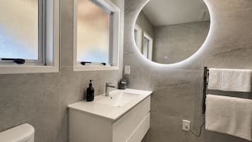 A modern bathroom with a white vanity, a round mirror, and a towel rack.