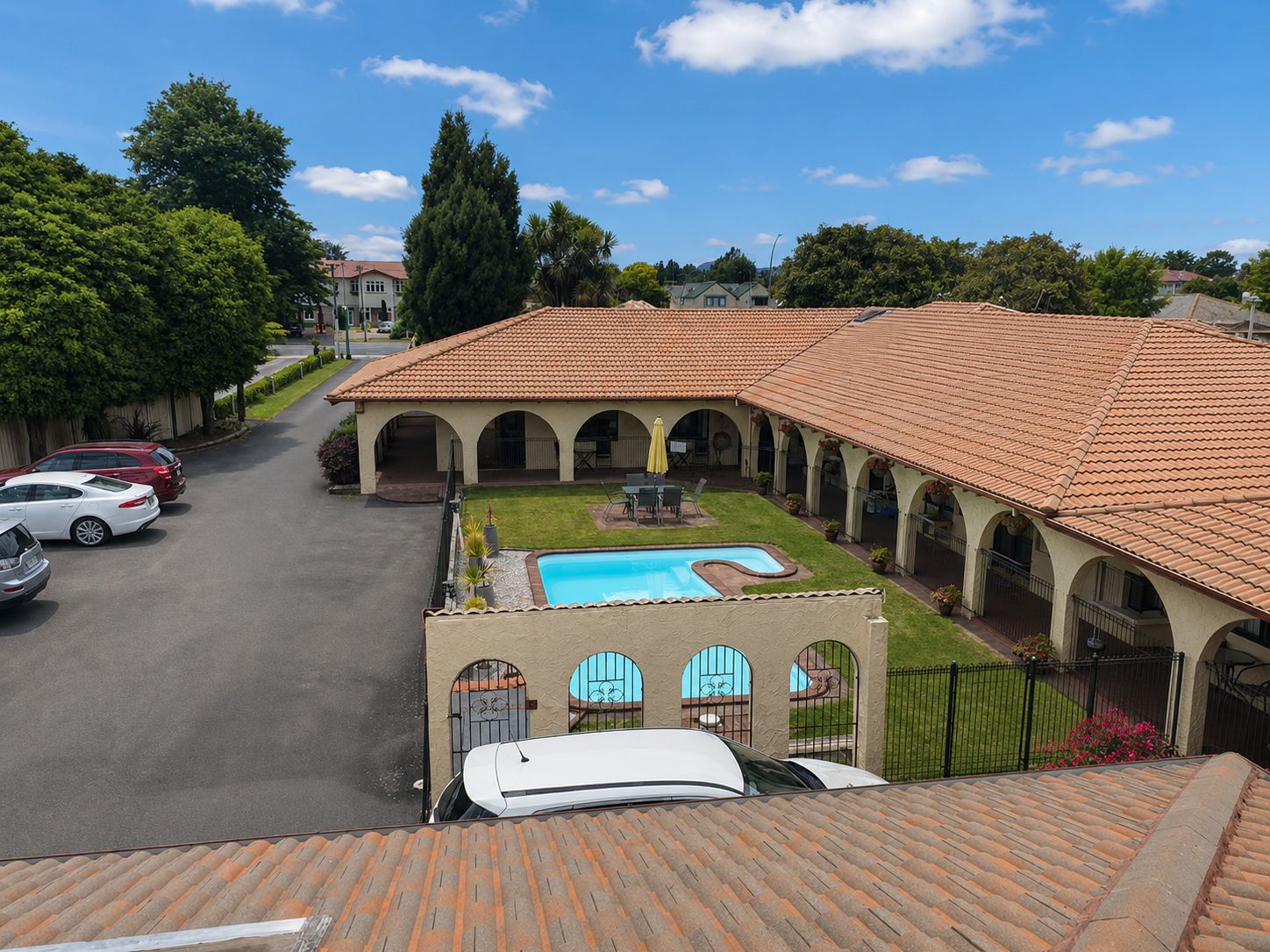A courtyard with a swimming pool, covered patio, and a car parked in the driveway.