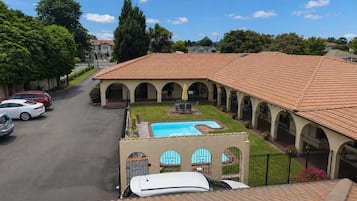 A courtyard with a swimming pool, covered patio, and a car parked in the driveway.