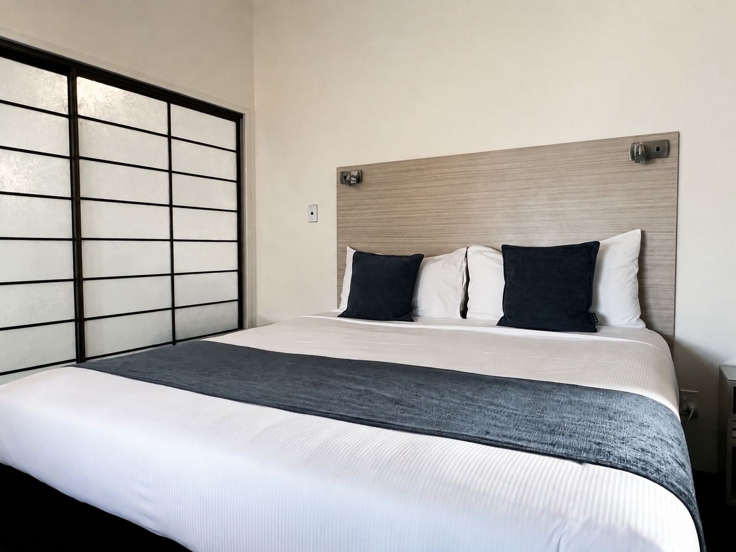 Habitación de hotel con cama, cabecera y ventana con diseño de celosía.