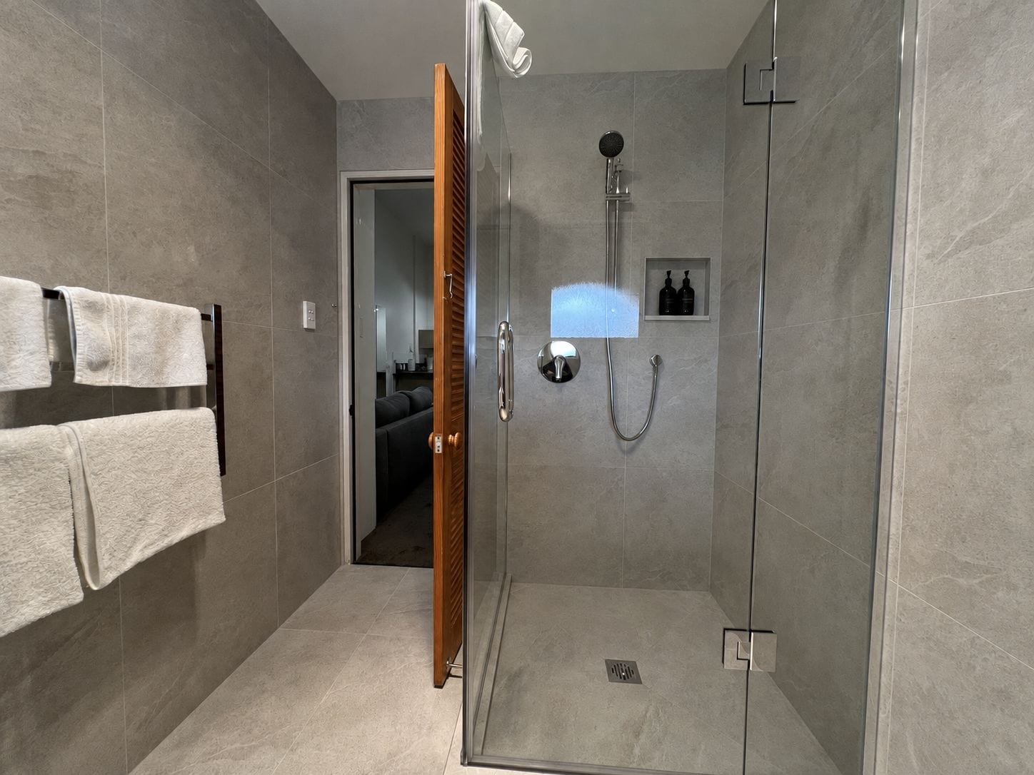 A modern bathroom with a glass shower enclosure, a towel rack with two towels, and a small shelf with toiletries.