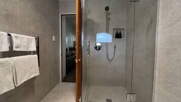 A modern bathroom with a glass shower enclosure, a towel rack with two towels, and a small shelf with toiletries.