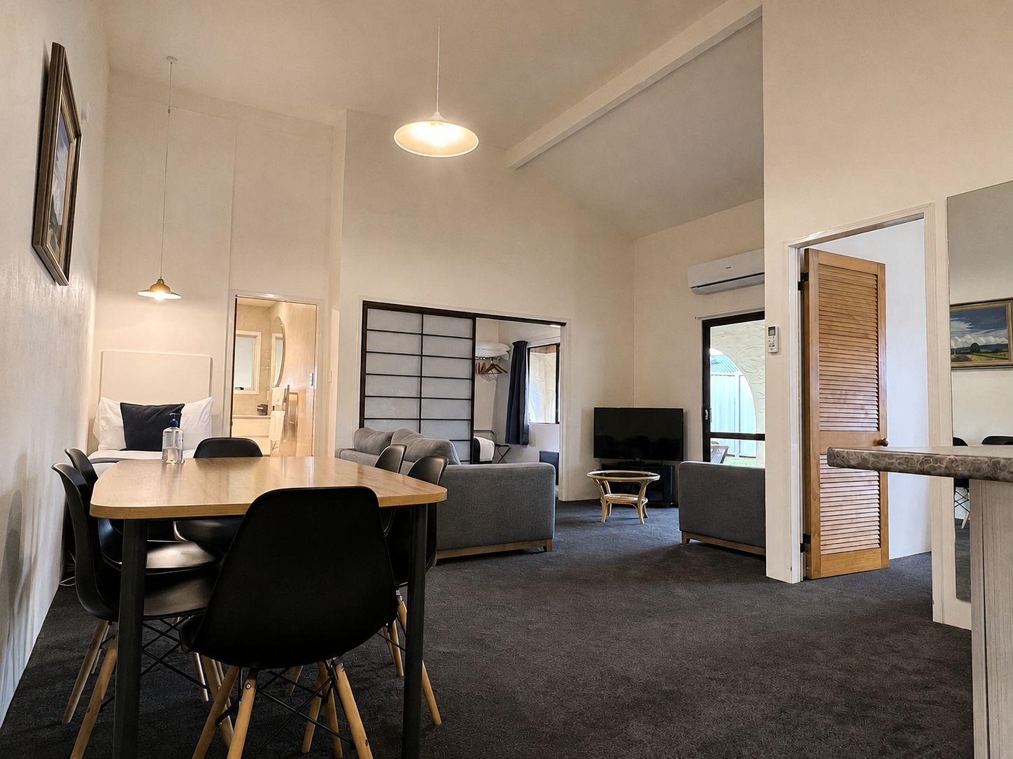 A modern hotel room with a dining area, a sofa, a TV, and a view of the outdoors.