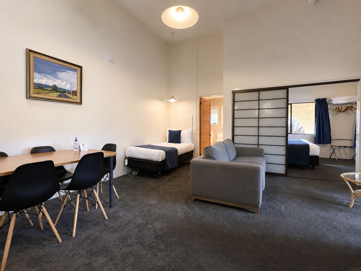 Habitación de hotel con una mesa de comedor, dos camas, un sofá y una puerta corrediza que da a otra habitación.