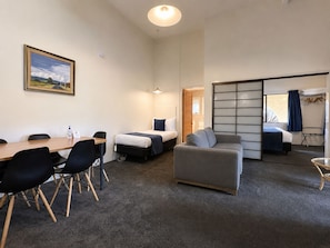 Habitación de hotel con una mesa de comedor, dos camas, un sofá y una puerta corrediza que da a otra habitación.