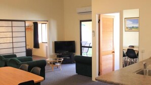A compact living space with a sofa, a TV, a dining table, and a kitchen area. - Captains Quarters Motor Inn (Cambridge)