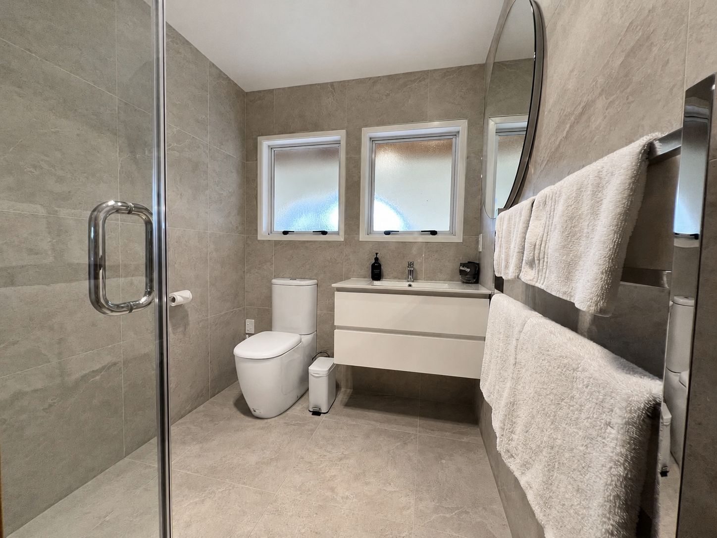 Ein modernes Badezimmer mit einer Glasdusche, einer Toilette, einem Waschbecken mit Spiegel darüber und einem Handtuchhalter.
