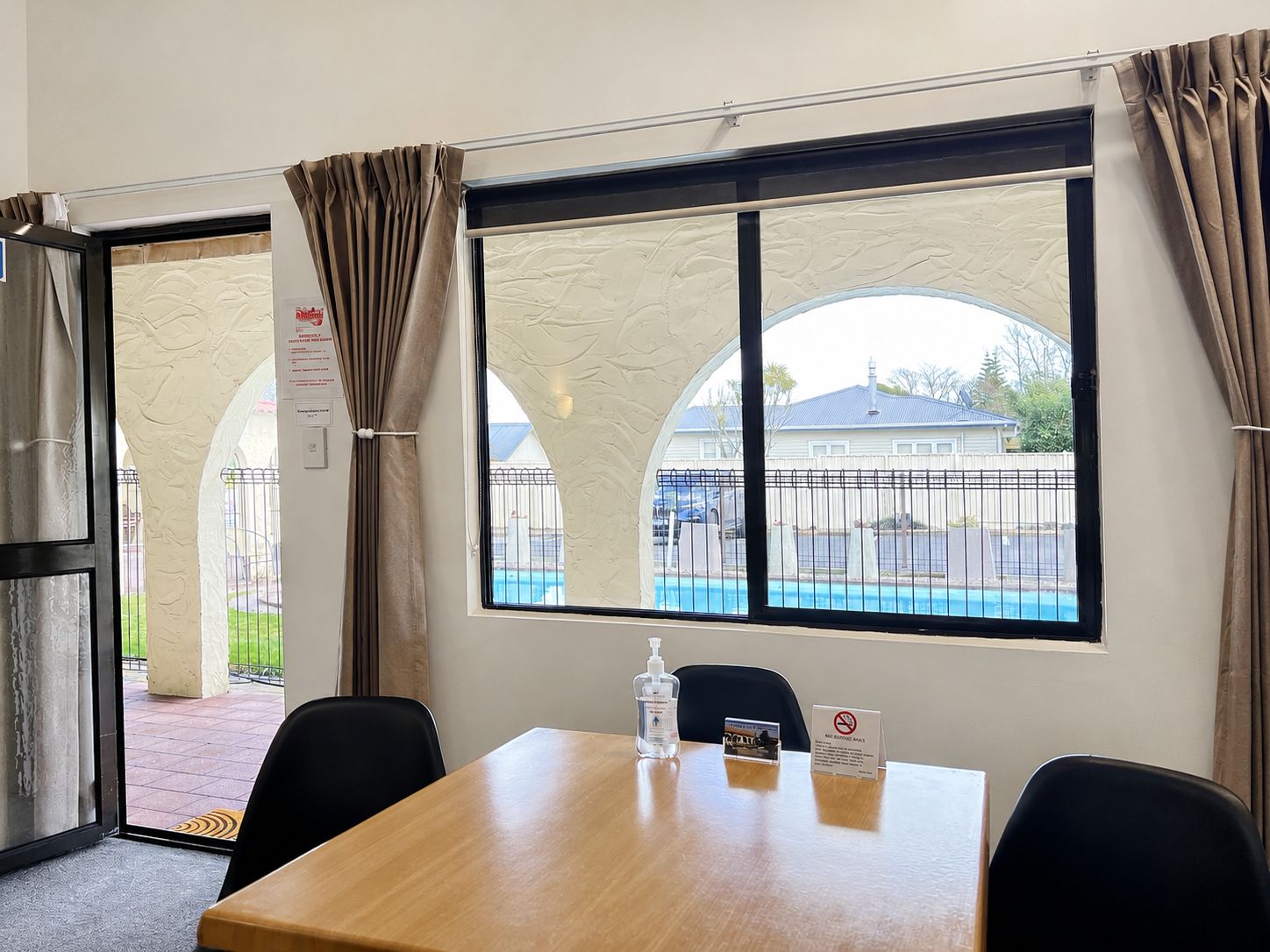 Ein Hotelzimmer mit einem Holztisch, zwei Stühlen, einem Fenster mit Blick auf einen Swimmingpool und einem Schild, das das Rauchen verbietet.