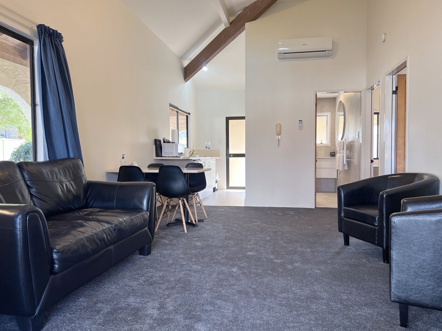 A modern living room with a leather sofa, a dining area with a table and chairs, and a kitchen visible through an open door.