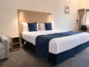 Habitación de hotel con una cama grande, mesitas de noche, una silla y una ventana con cortinas.