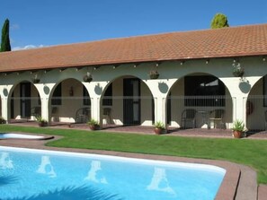Zona junto a la piscina con techo de baldosas, mobiliario exterior y una pileta.