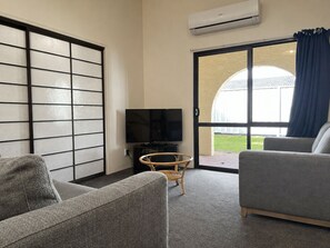 Una habitación con sofá, televisión, una silla de mimbre y un ventanal con cortinas.