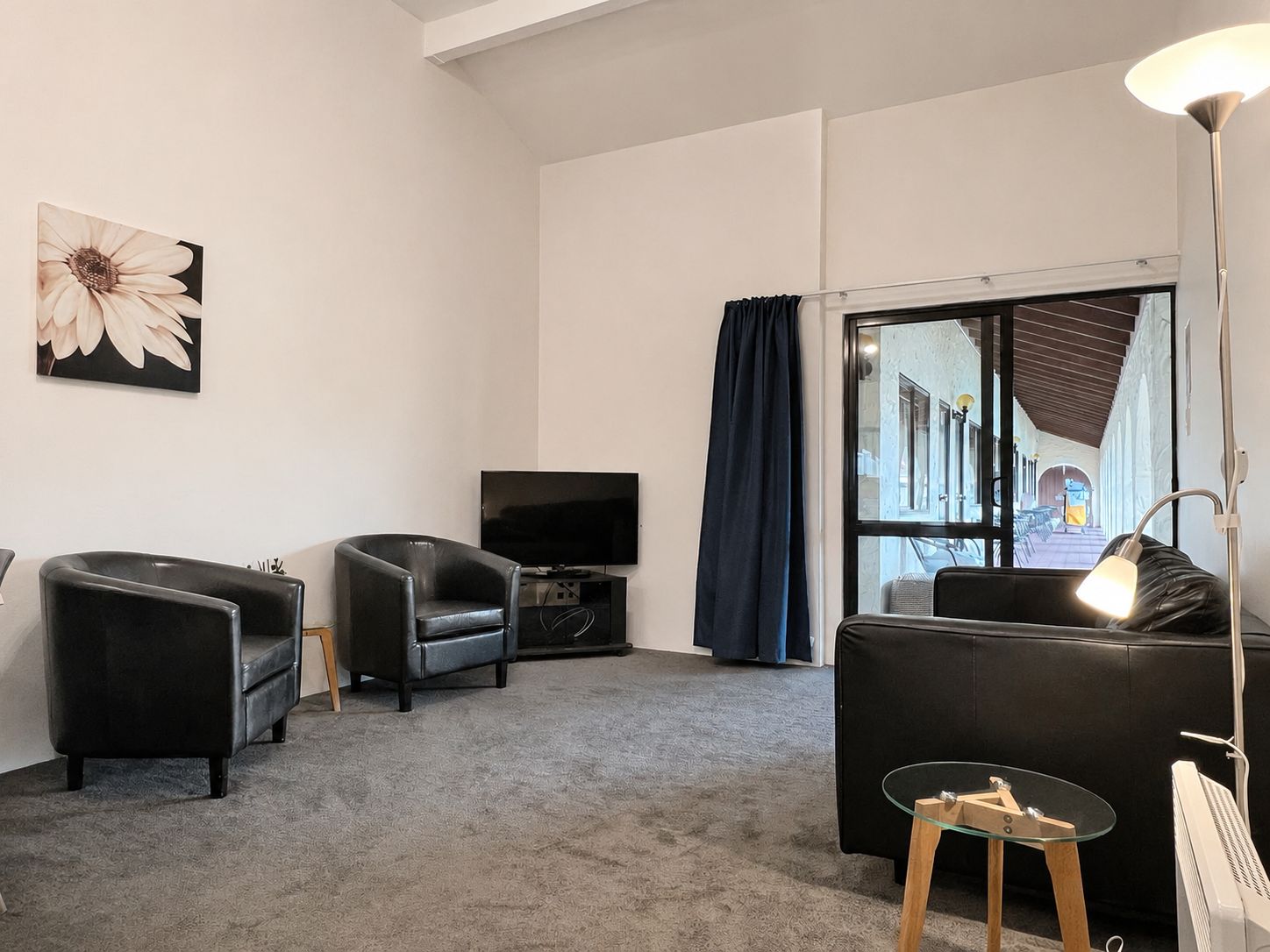 Ein modernes Wohnzimmer mit einem Flachbildfernseher, zwei Ledersofas, einem Glastisch und einem großen Fenster mit Vorhängen.