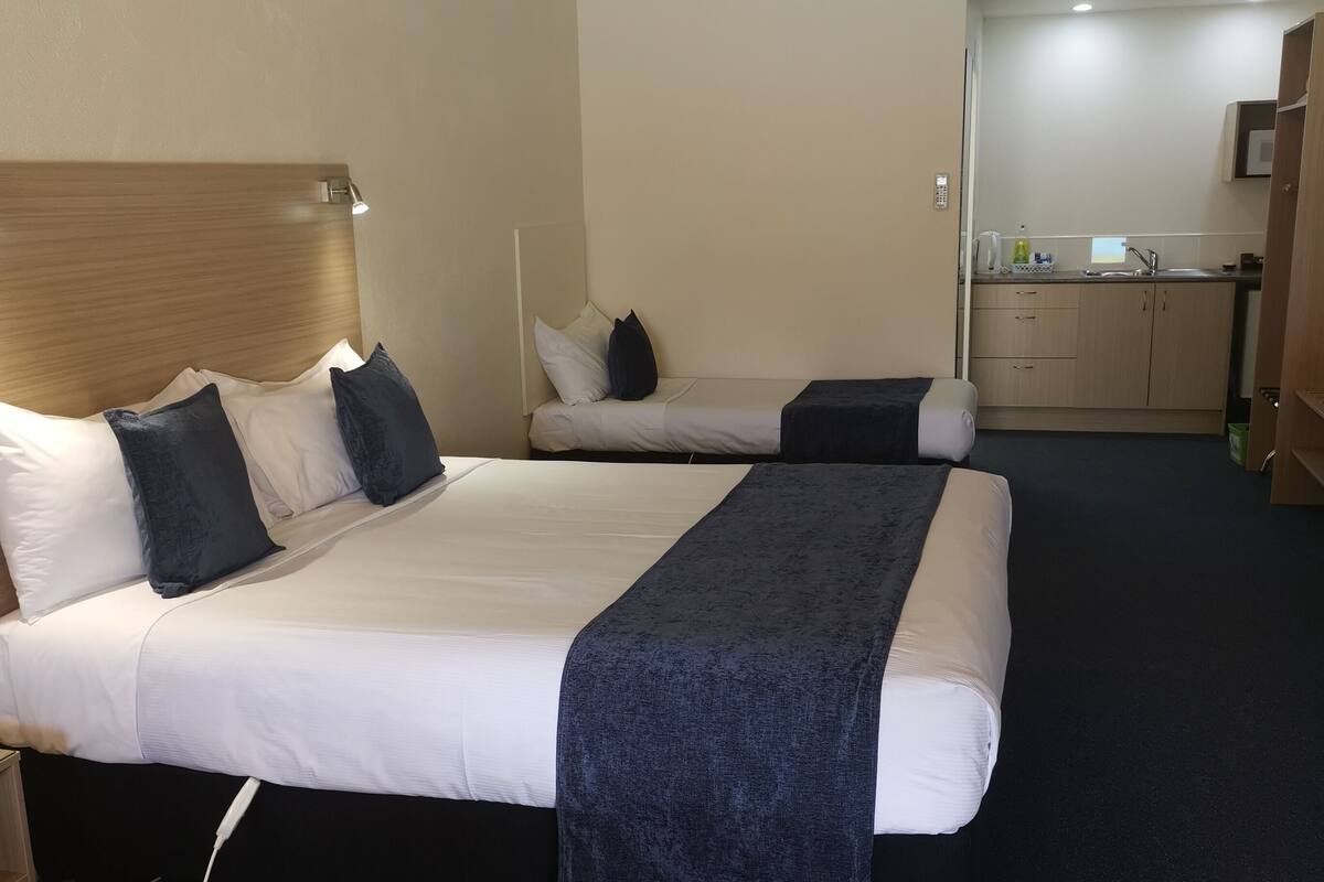 Habitación de hotel con dos camas, un escritorio, kitchenette y unidad de aire acondicionado.
