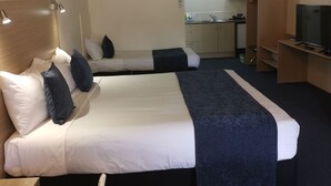 A hotel room with two beds, a desk, a TV, a wardrobe, and a kitchenette in the background. - Captains Quarters Motor Inn (Cambridge)