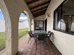 Un patio techado con mesa y sillas, techo de madera y vista a un jardín trasero cercado.