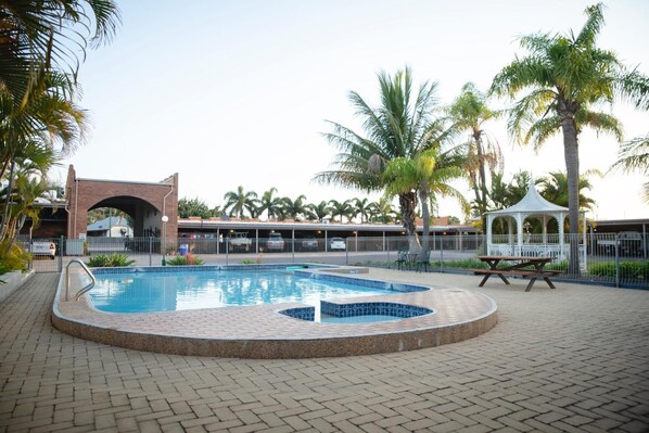 A swimming pool with a brick border, a gazebo, and palm trees.