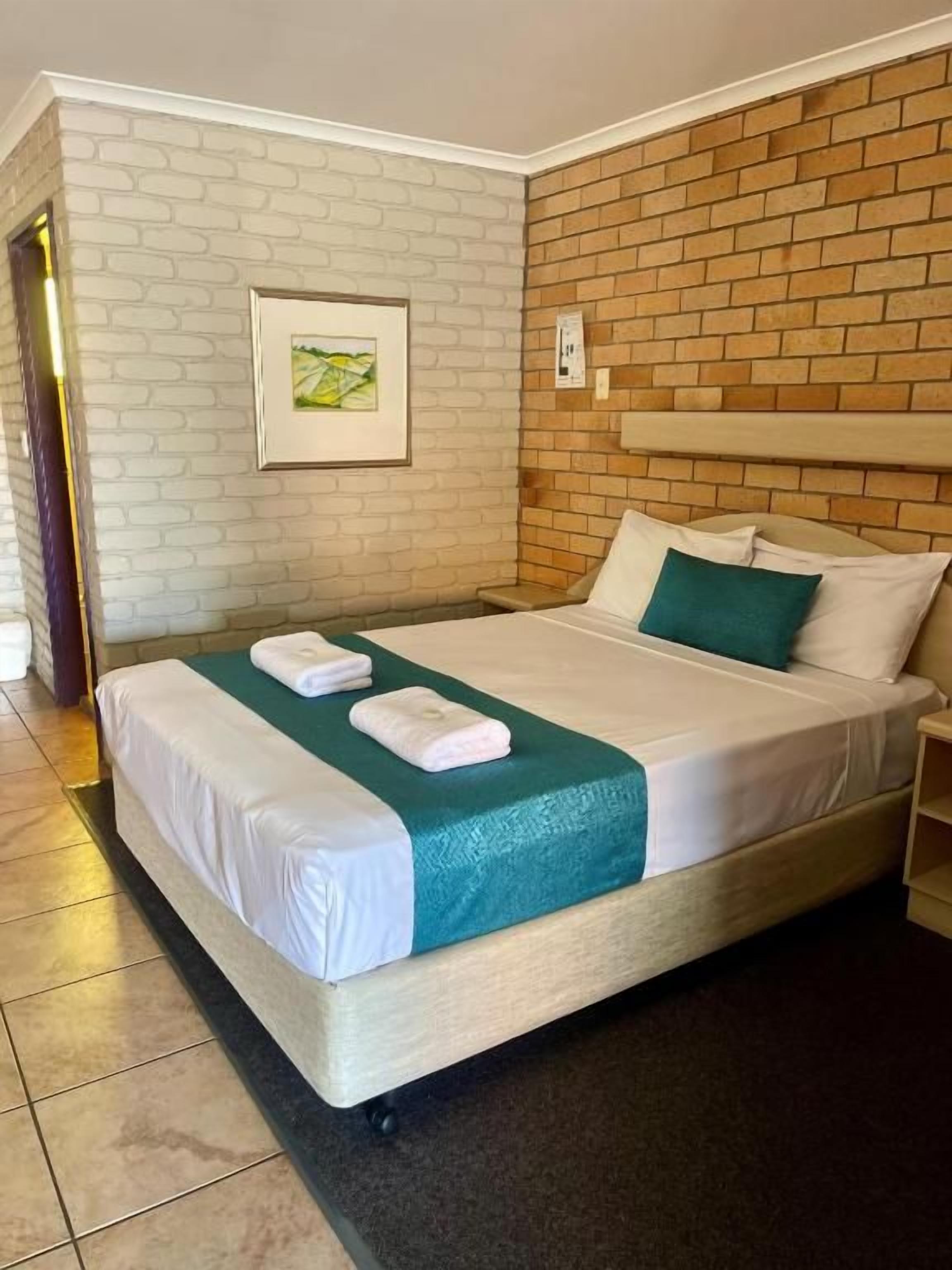 Een hotelkamer met een met baksteen patroon bedekte muur, een bed met witte lakens en een ingelijst schilderij aan de muur.