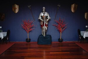 Una habitación con piso de madera, una mesa con mantel blanco y dos plantas en macetas con follaje rojo.