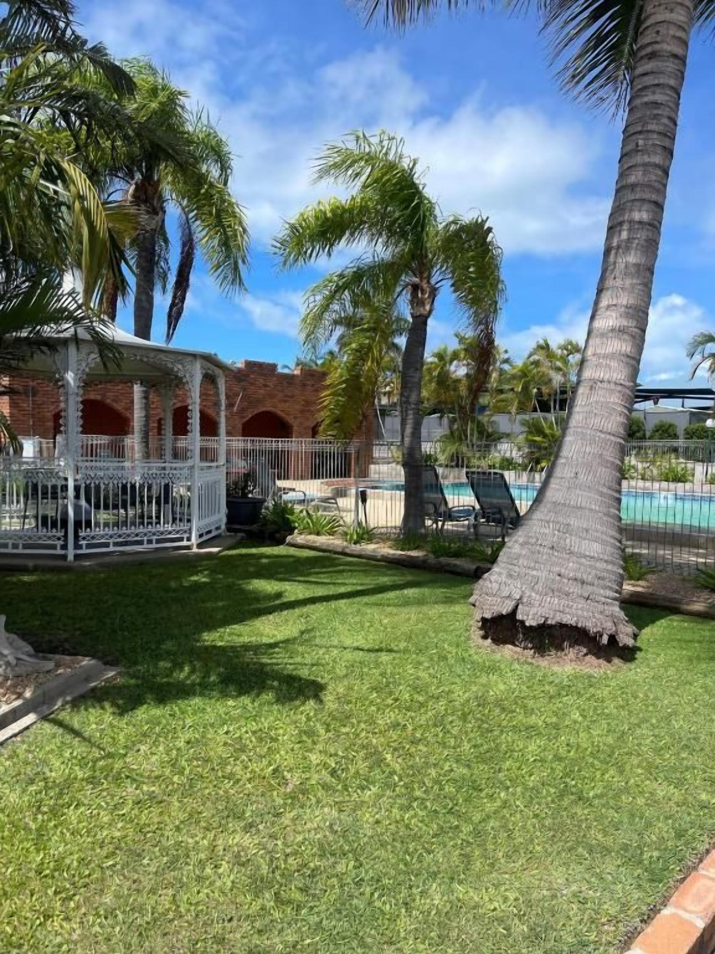 A well-maintained lawn with a palm tree, a gazebo, and a swimming pool in the background.