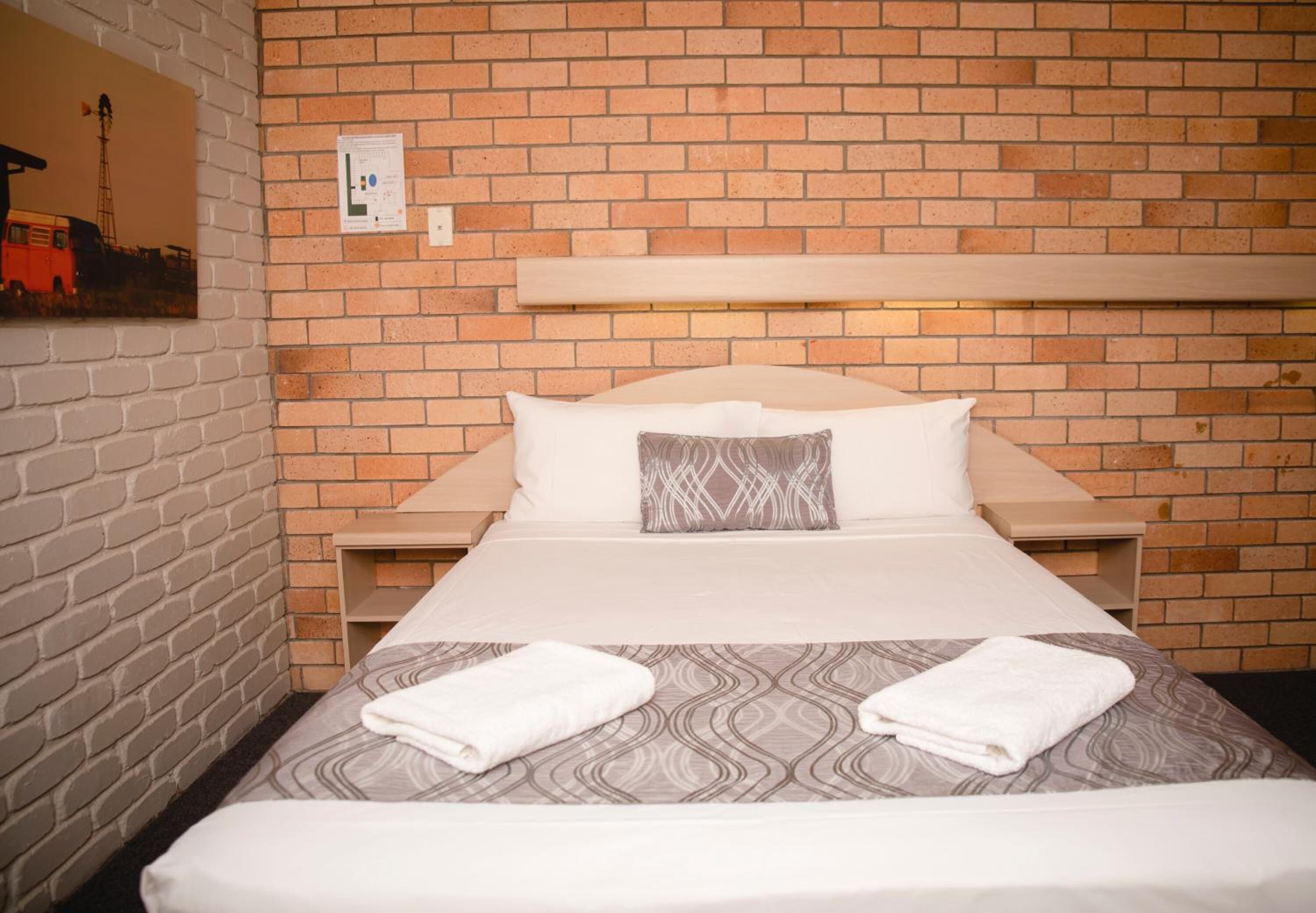 Habitación de hotel con pared de ladrillo, cama con colcha estampada, dos toallas blancas y un cuadro en la pared.