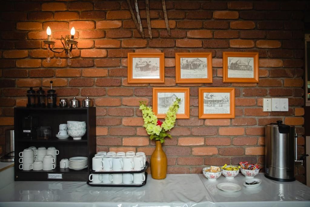 Una barra de desayuno con pared de ladrillo, cuadros enmarcados, un jarrón con flores y diversos productos para el desayuno.