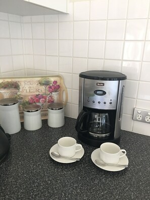 A kitchen with a Breville coffee maker, three white containers, and two white cups on a granite countertop. - Sabina On Little Myers (Geelong)