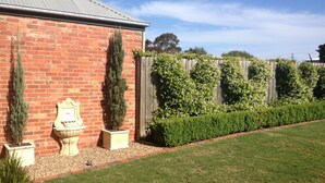 A brick building with a metal roof, surrounded by a well-maintained garden with hedges and a lawn. - Sabina On Little Myers (Geelong)