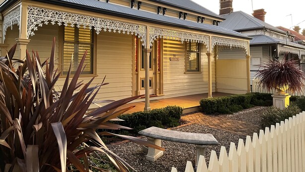 A two-story house with a decorative porch, a driveway, and a white picket fence. - Sabina On Little Myers (Geelong)