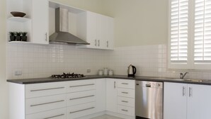 A modern kitchen with white cabinetry, a stainless steel dishwasher, and a gas stove. - Sabina On Little Myers (Geelong)