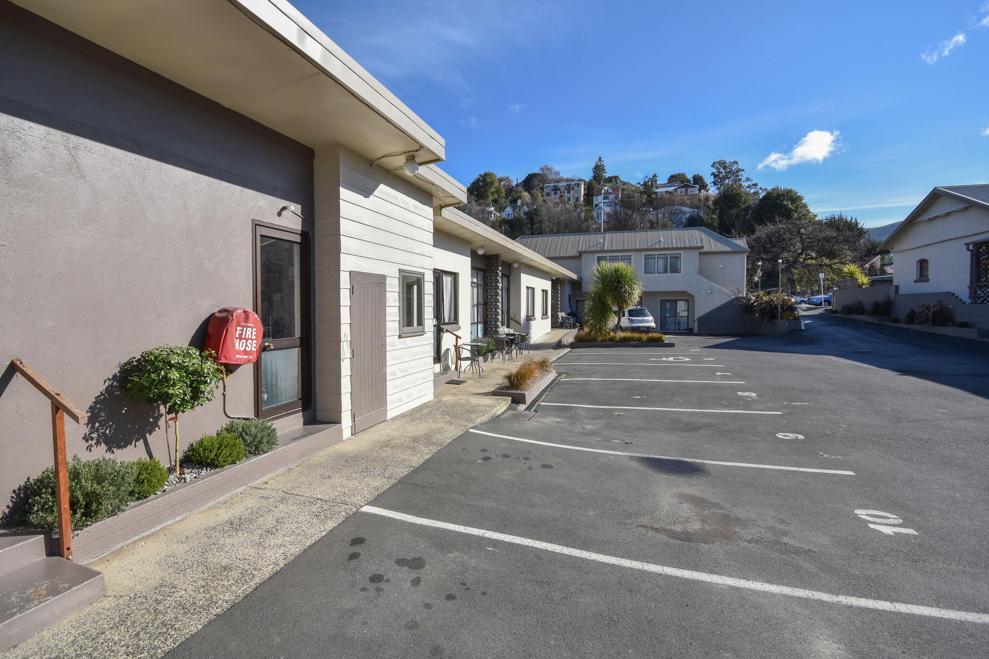 A parking lot with marked spaces, a fire hose mounted on the building, and a clear view of the surrounding neighborhood.