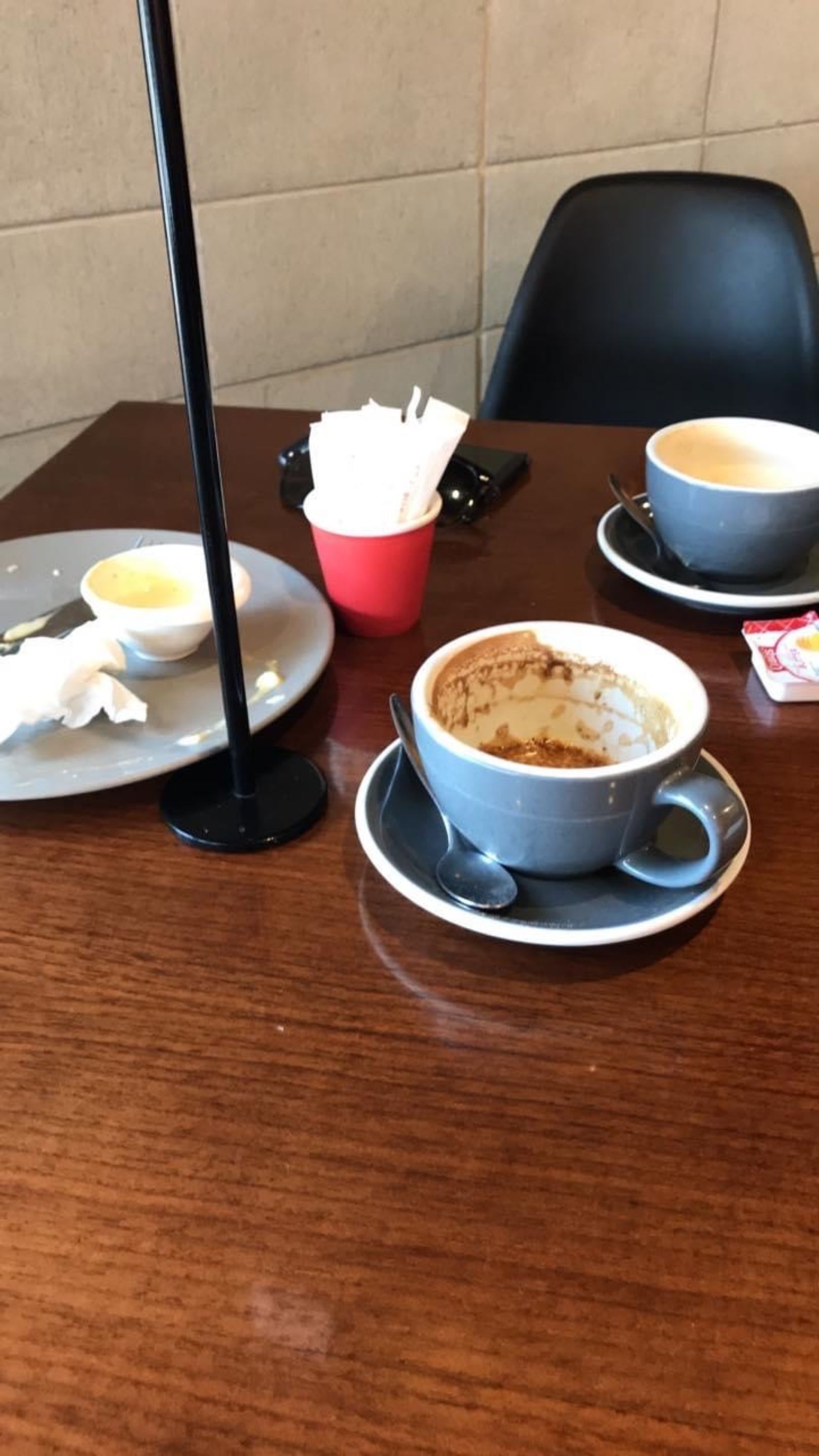 Uma mesa com uma xícara de café, uma caneca vermelha e um smartphone.