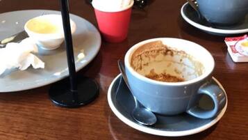A table with a cup of coffee, a red cup, and a smartphone on it.