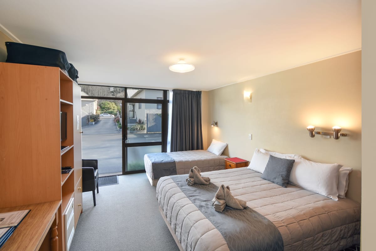A hotel room with two beds, a wooden wardrobe, a desk, and a view of the street outside.