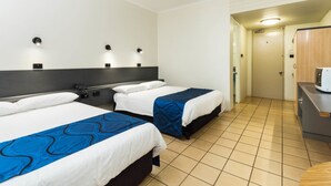 Camera d'albergo con due letti, angolo cottura e bagno parzialmente visibile da una porta aperta.