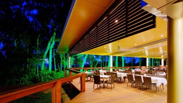 Un'area pranzo all'aperto con tavoli e sedie, circondata da un pontile e una ringhiera in legno, con vista su alberi e un cielo notturno.