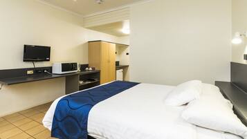Habitación de hotel con cama, escritorio con computadora y microondas, armario y televisor montado en la pared.