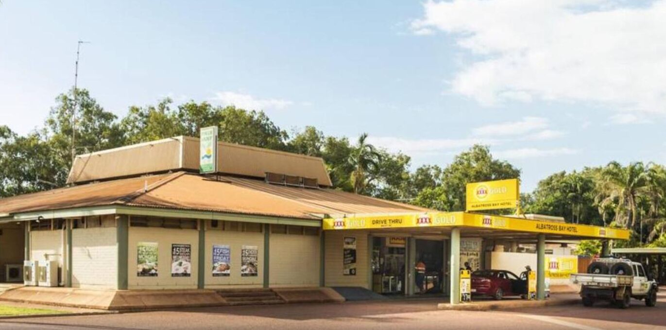 A small, single-story building with a flat roof and a covered front area. There are signs indicating a drive-thru service and a hotel named "Albatross Bay Hotel".