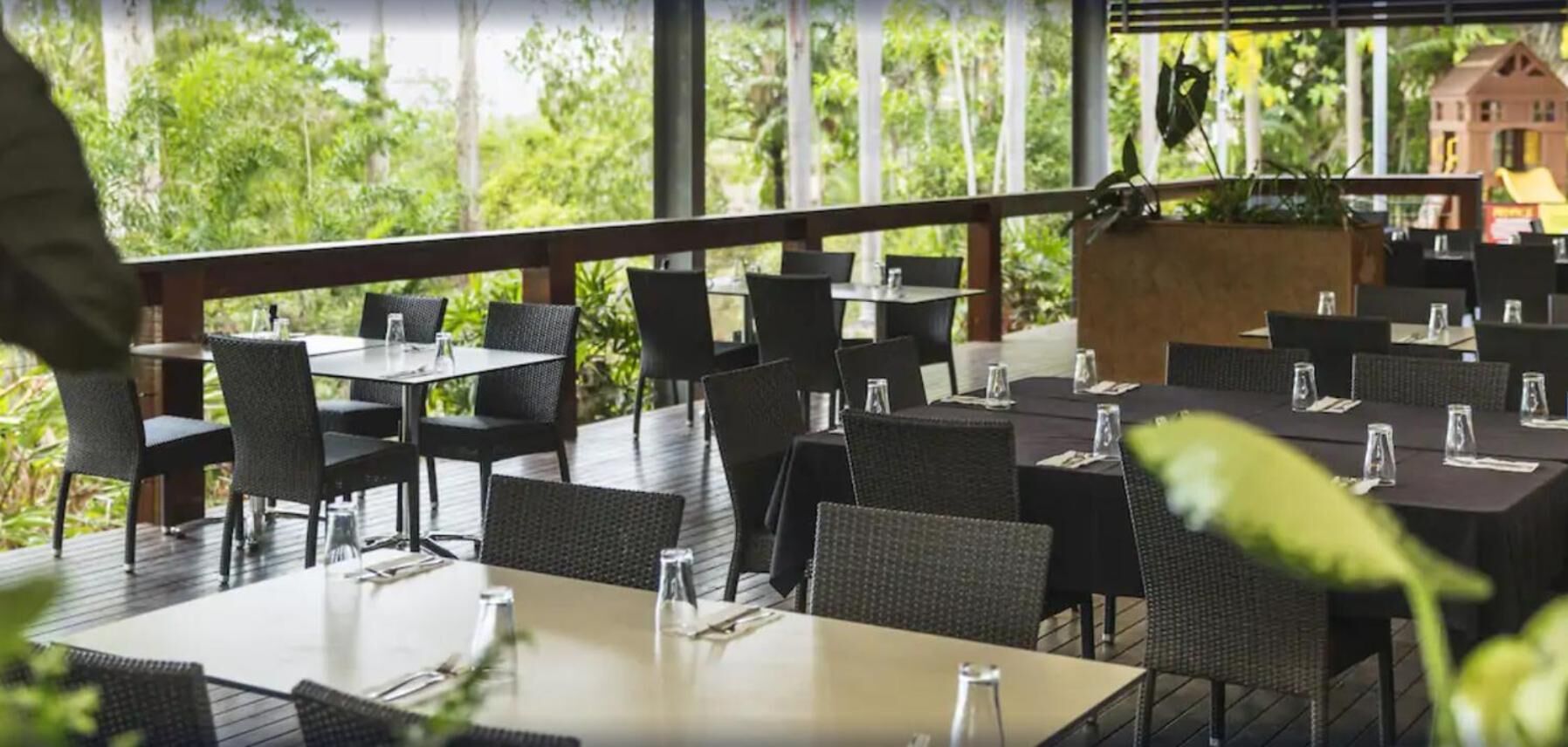 Un restaurante al aire libre con mesas y sillas, rodeado de vegetación y una terraza de madera.