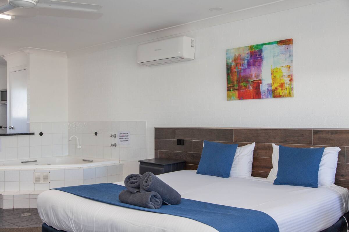 A hotel room with a large bed, a bathtub, and a colorful abstract painting on the wall.