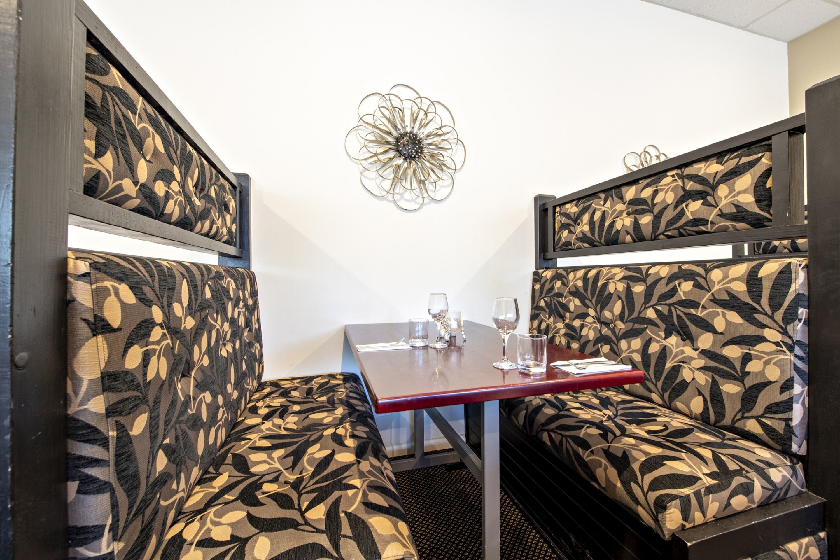 Un comedor con asientos tipo cabina estampados, una mesa con vasos y cubiertos, y un elemento decorativo en la pared.