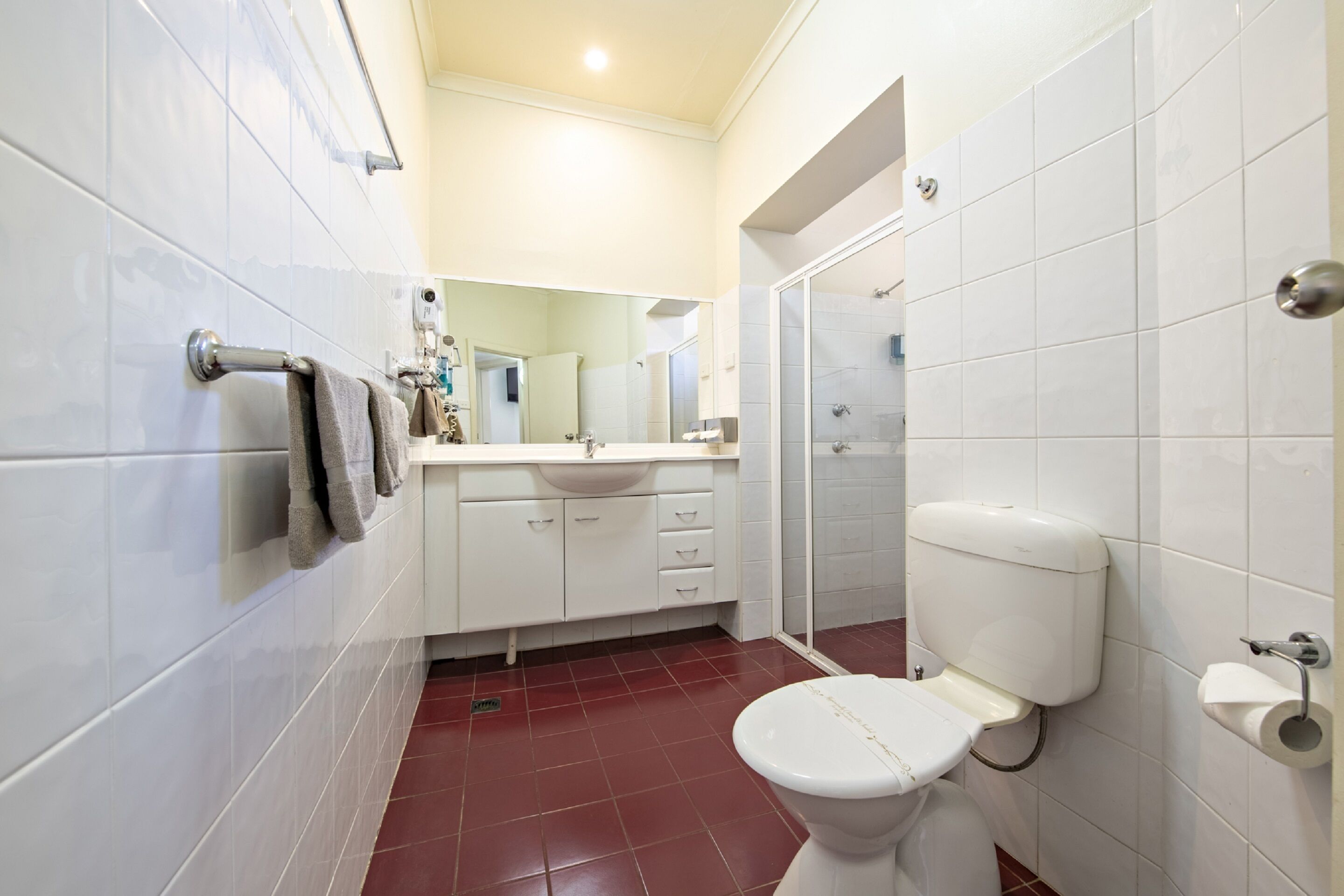 A bathroom with white tiles, a white toilet, a sink, and a shower area.