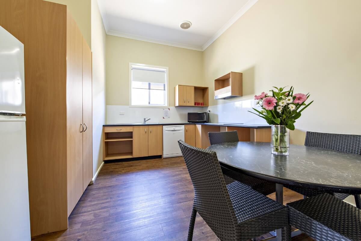 A modern kitchen with wooden cabinets, a dining table with wicker chairs, and a vase of flowers on the table.
